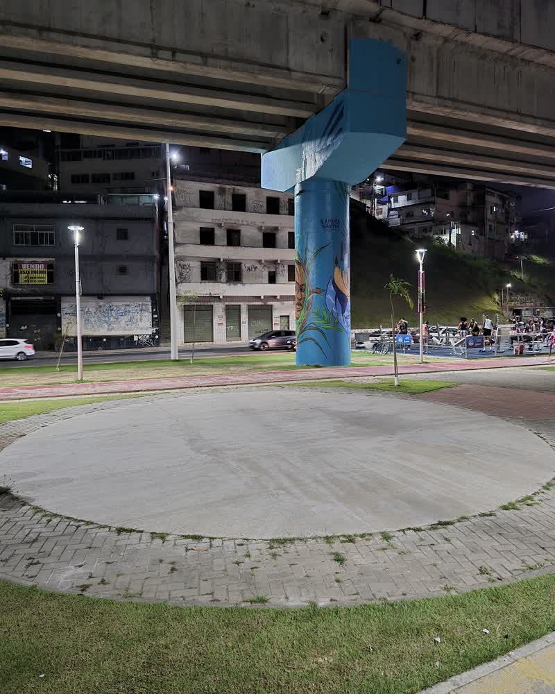 O círculo de concreto onde a roda se monta, vazio, embaixo do viaduto da Avenida Bonocô: a coluna azul com mural pintado ao centro, a avenida e os prédios ao fundo.